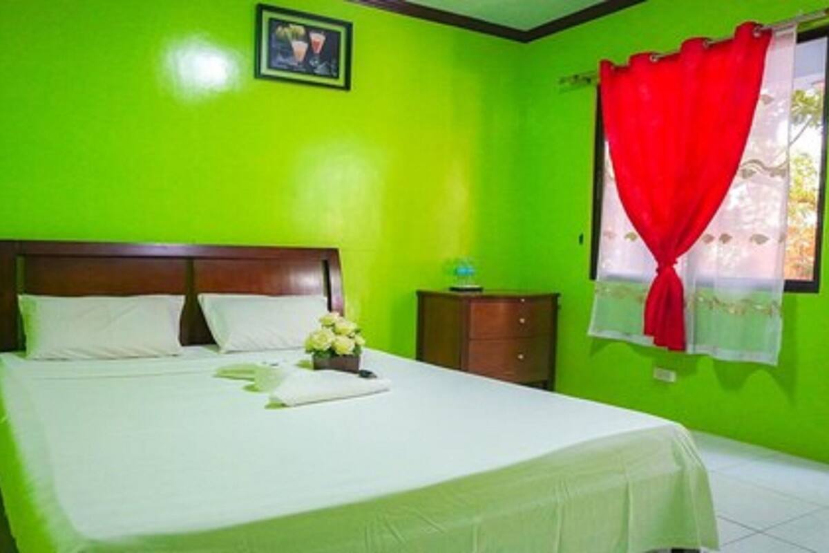 A room with a bed, a nightstand, and a window with red curtains.