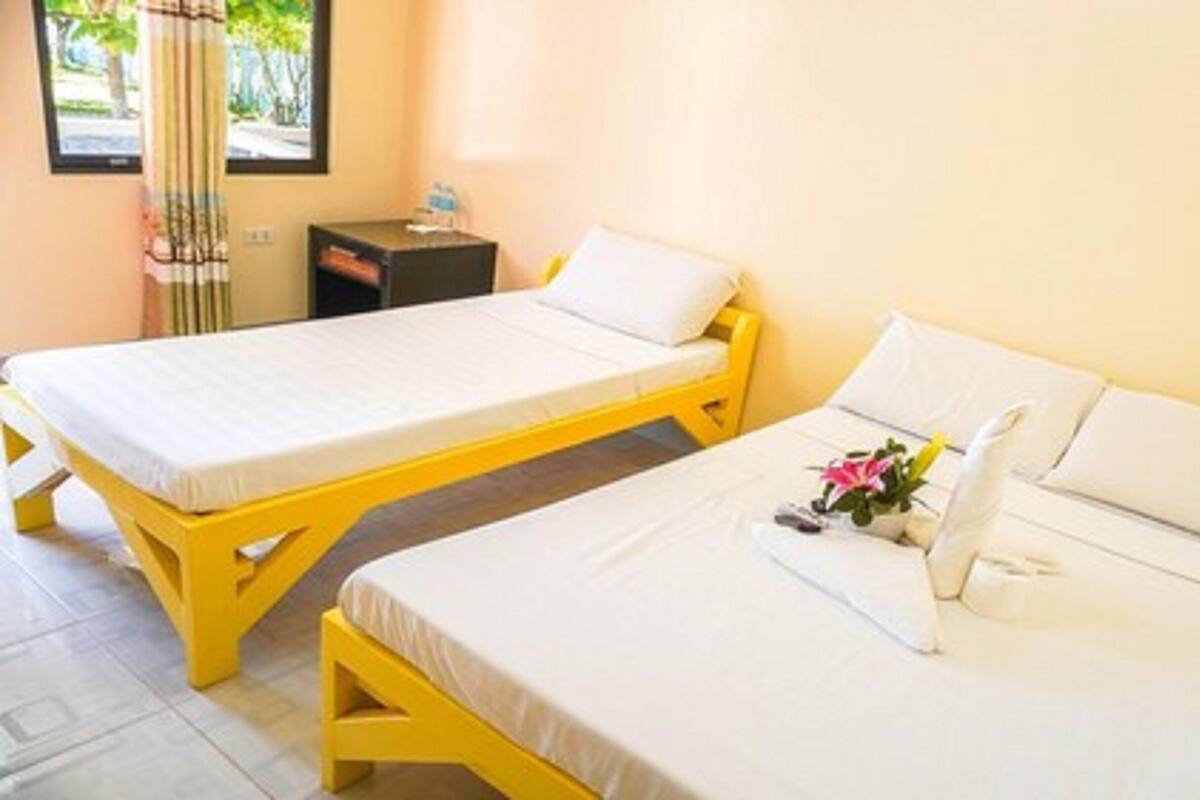 Two single beds with white linens, a small table with a lamp, and a window with curtains.