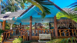 Une structure en bois surmontée d’un toit de chaume, entourée d’une végétation tropicale.