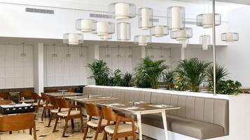 A modern restaurant interior with a long counter, multiple seating options including booths and tables, and a variety of pendant lights.