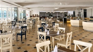 Un vaste espace dédié à la salle à manger, avec de nombreuses tables et chaises, un bar central et un lustre.