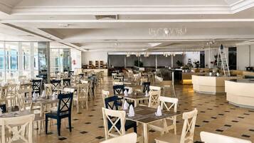 Un comedor espacioso con varias mesas y sillas, una barra central y una araña.