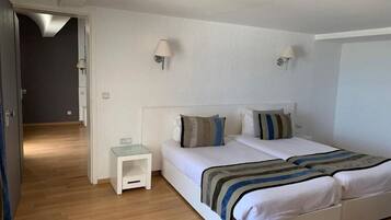 A bedroom with two beds, a small bedside table, and wall-mounted lamps.