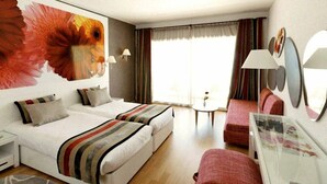 Une chambre d’hôtel avec deux lits, un canapé, une petite table et une grande œuvre d’art florale accrochée au mur.
