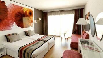 Habitación de hotel con dos camas, un sofá, una mesita y un cuadro grande con motivos florales en la pared.