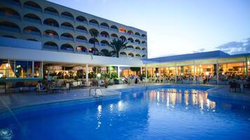A hotel with a swimming pool, outdoor seating, and a covered area with tables and chairs.
