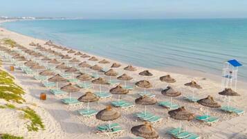 A beach with rows of sun loungers and thatched umbrellas.