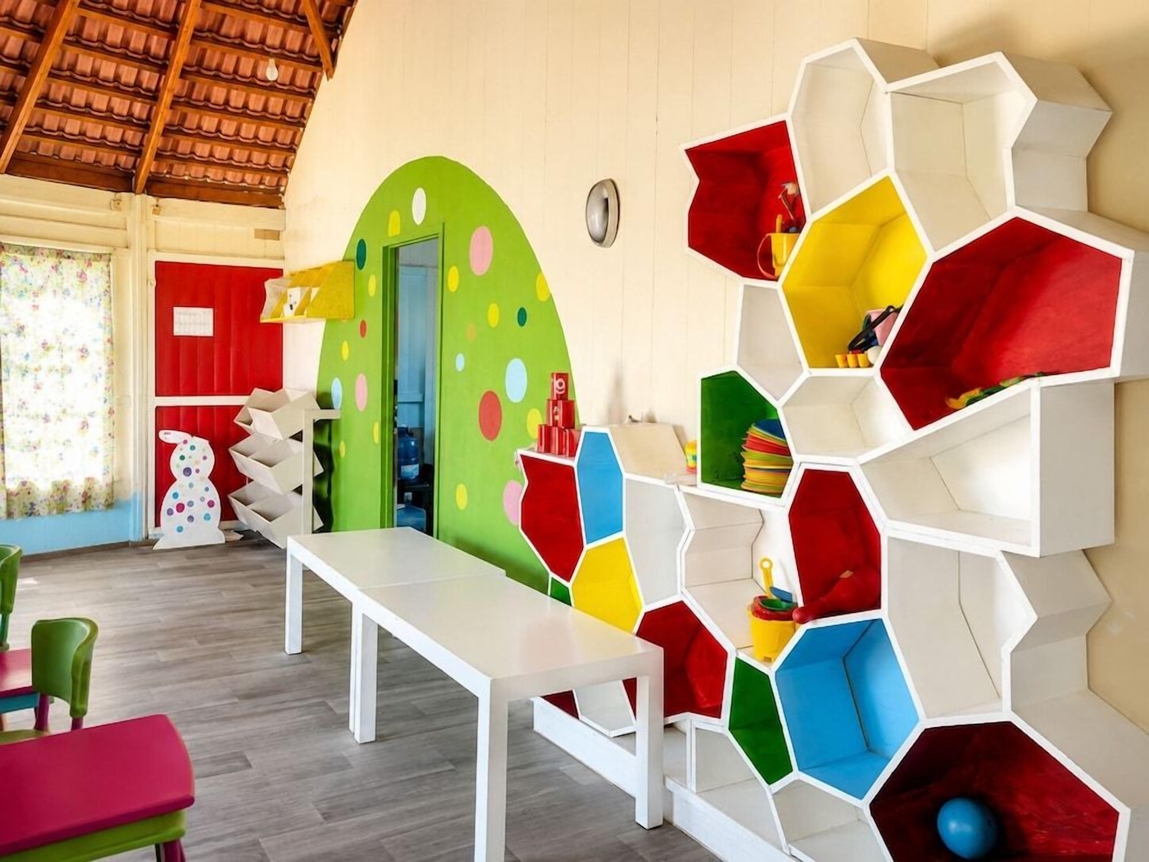 A room with a white table, colorful hexagonal storage units, a red door, and a green wall with circular patterns.