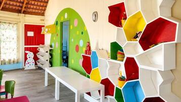A room with a white table, colorful hexagonal storage units, a red door, and a green wall with circular patterns.