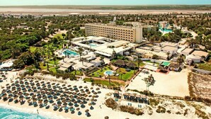 Un complexe hôtelier comprenant plusieurs bâtiments, une grande piscine et une plage aménagée avec des parasols.