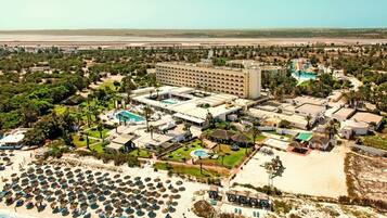 Un resort con varias edificaciones, una piscina grande y una zona de playa con sombrillas.