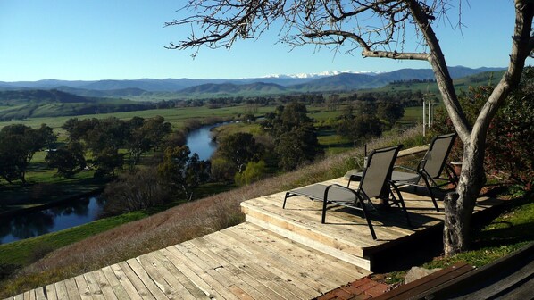 A wooden deck with two chairs overlooking a river and a valley with distant mountains.