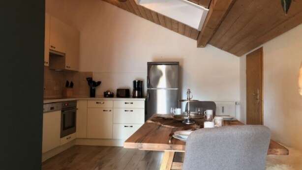 A compact kitchen with wooden cabinets, a stainless steel refrigerator, and a dining table with chairs. - Ferienwohnung Hochgern (Grassau)