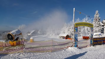 A snow-covered ski resort entrance with a ski lift and a sign for 'SKISCHULE ALTASTENBERG'.