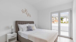 A bedroom with a bed, nightstand, and a view of the outside through a large window. - Apartments Villa Salona Sky (Solin)