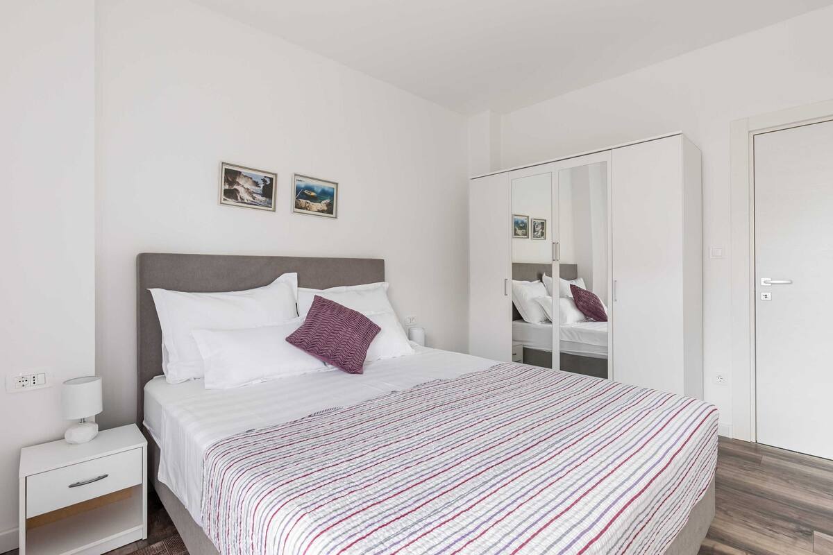 A modern bedroom with a bed, white nightstand, and a wardrobe with a mirror.