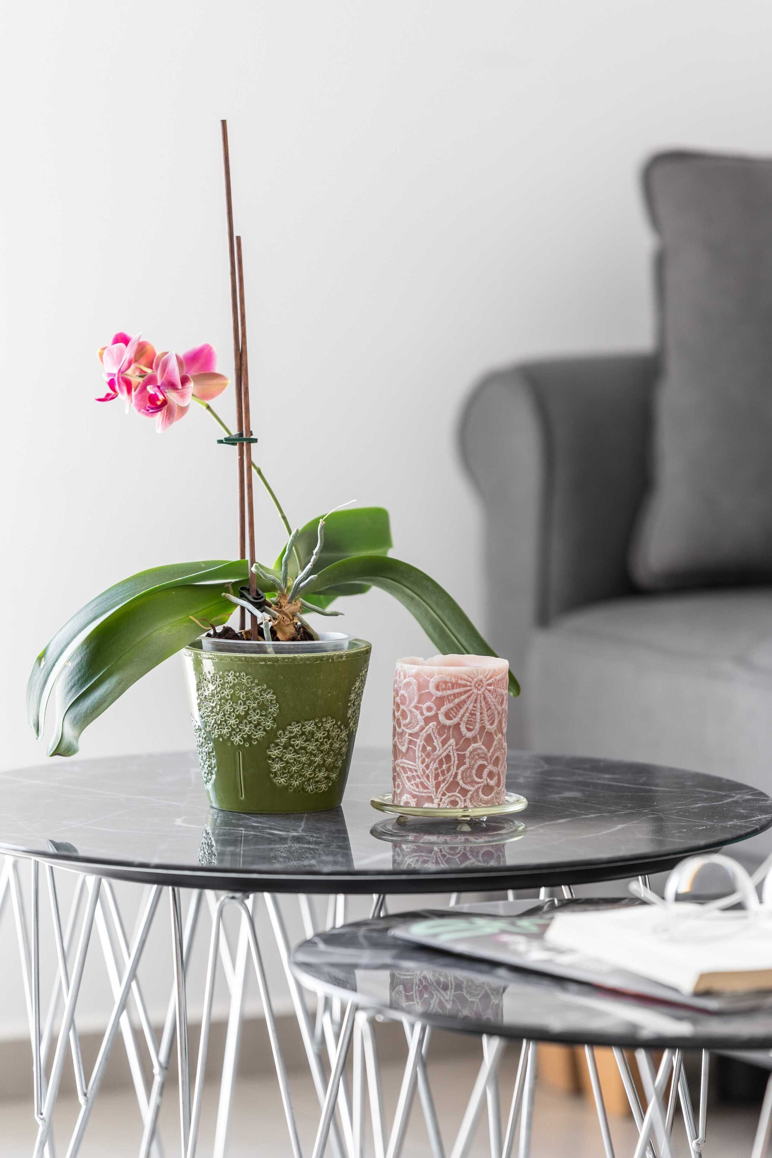 A round glass table with a potted orchid and a candle.