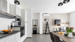 A modern kitchen with a microwave, oven, and coffee maker. There is a dining table with chairs and a vase of flowers. - Apartments Villa Salona Sky (Solin)