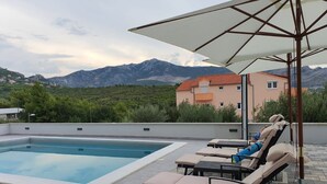 A rooftop pool area with lounge chairs and an umbrella, overlooking a mountainous landscape. - Apartments Villa Salona Sky (Solin)