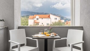 A balcony with two white wicker chairs, a small table with a book, a pitcher of orange juice, a glass of orange juice, and a plate of croissants. - Apartments Villa Salona Sky (Solin)
