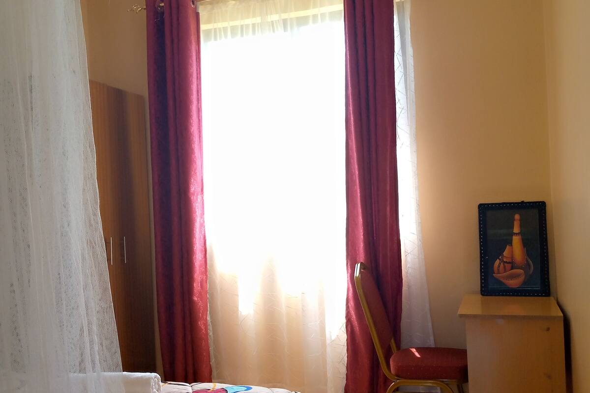 A bedroom with a bed, a chair, a desk, and a window with curtains.