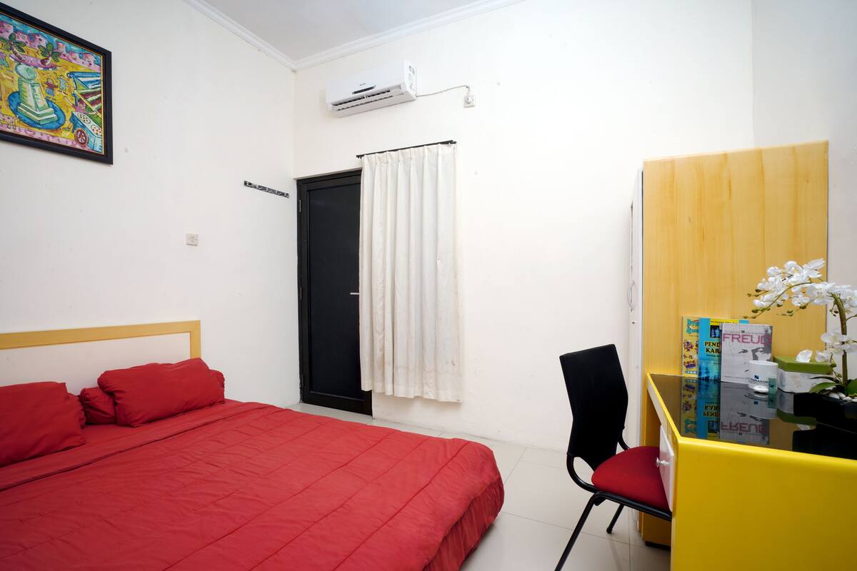 A room with a bed, a desk, a chair, a door, and an air conditioner.