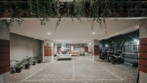 A gated entrance with a paved driveway leading to a white car parked inside. - Dparagon Kemuning - Campus Accommodation (Depok)