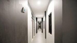 A narrow, well-lit hallway with a tiled floor, flanked by walls with doors and windows. - Dparagon Kemuning - Campus Accommodation (Depok)