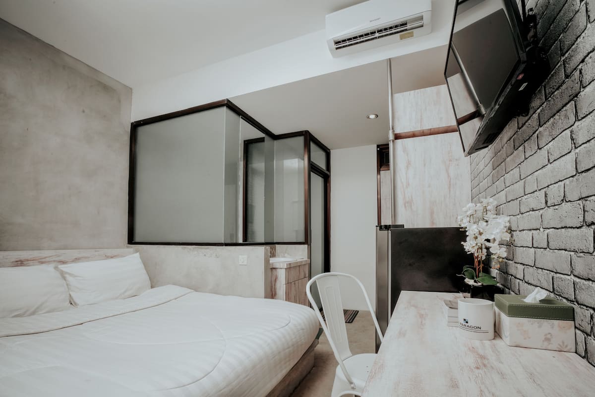 A modern hotel room with a bed, a small table with a tissue box, a chair, and a TV mounted on the wall.