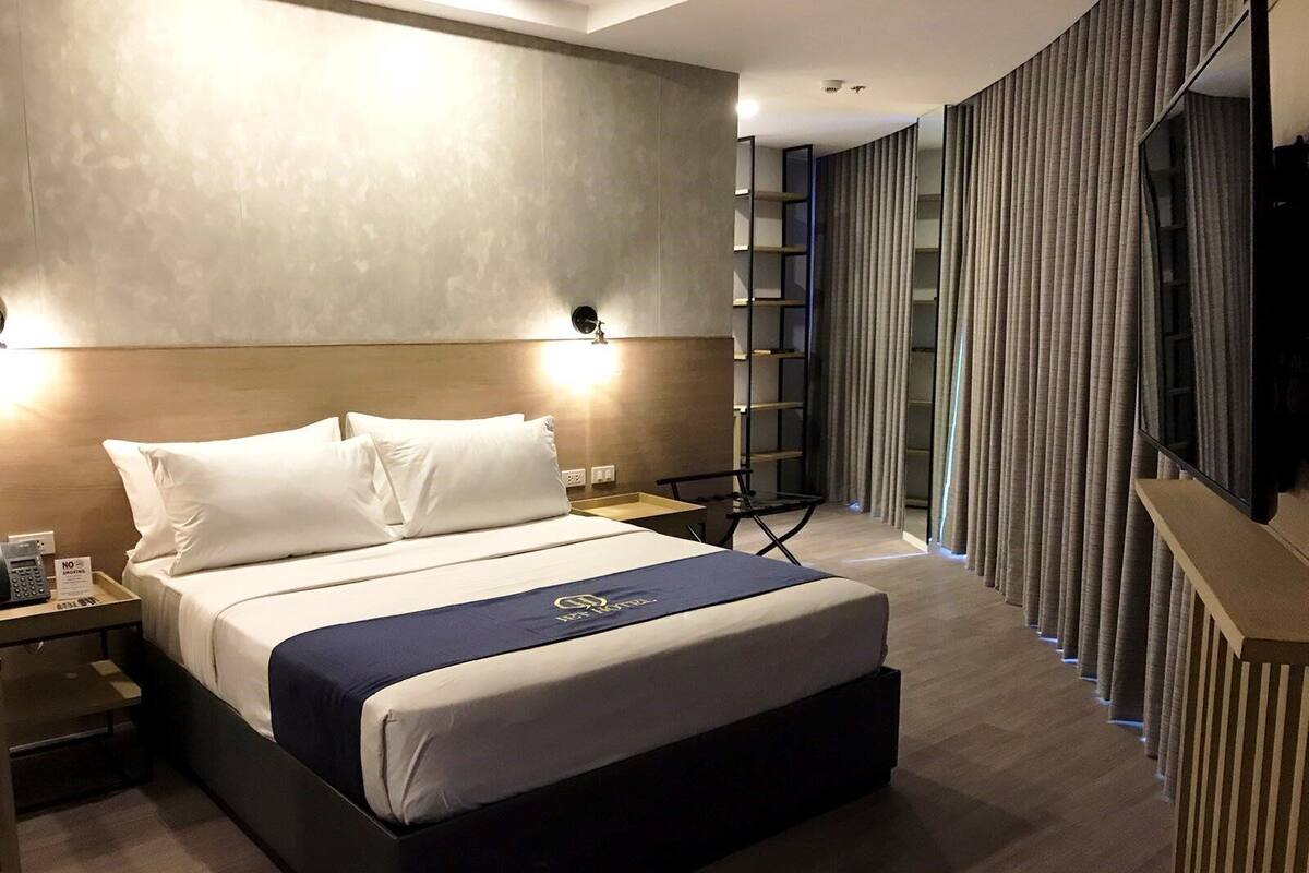 Quarto de hotel moderno com uma cama grande, uma mesa com telefone e uma TV em um suporte.