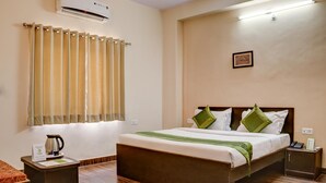 Una habitación de hotel con cama, mesitas de noche, cafetera y ventana con cortinas.
