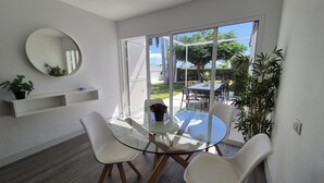 Een moderne eethoek met een glazen tafel en witte stoelen, een ronde spiegel aan de muur en uitzicht op de omgeving.