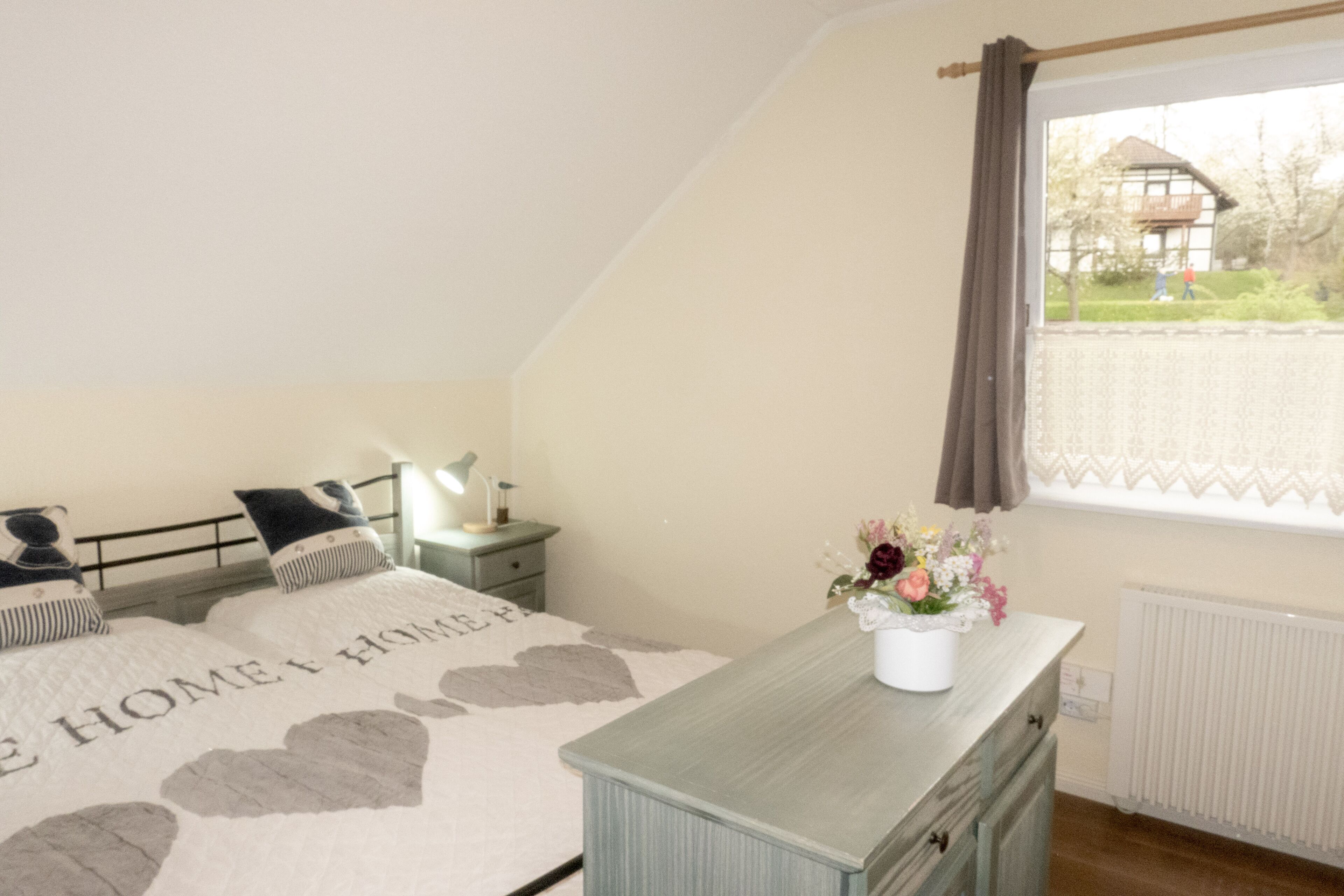 Ein Schlafzimmer mit Bett, Nachttisch, Lampe, Schminktisch, Fenster und Blick ins Freie.