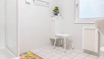Ein Badezimmer mit weißen Fliesen, einer Dusche, einem WC, einem Heizkörper und einem Fenster.