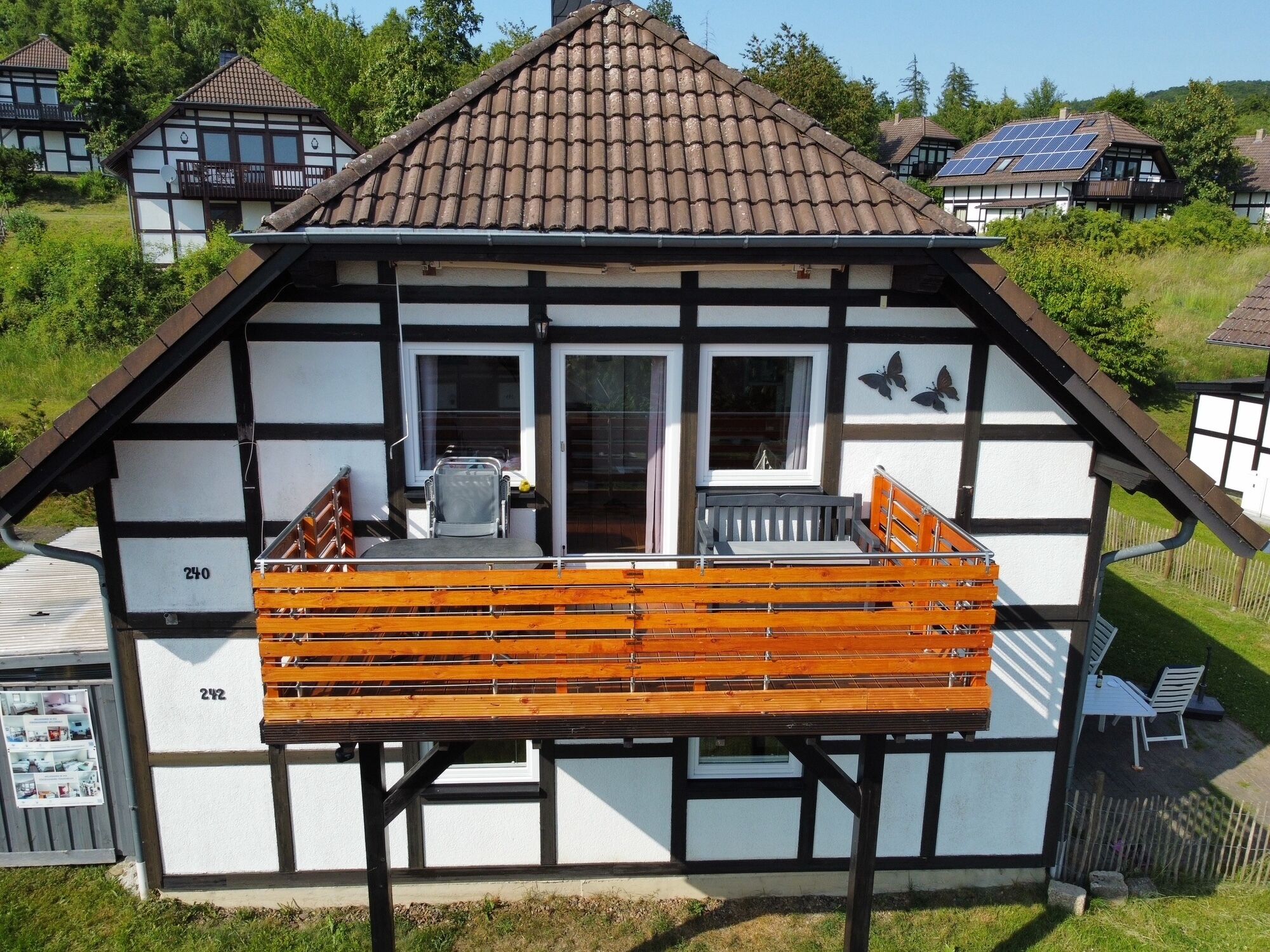 Ein traditionelles Fachwerkhäuschen mit Balkon, mit den Hausnummern 240 und 242, mit einer hölzernen Bank und einem kleinen Tisch.