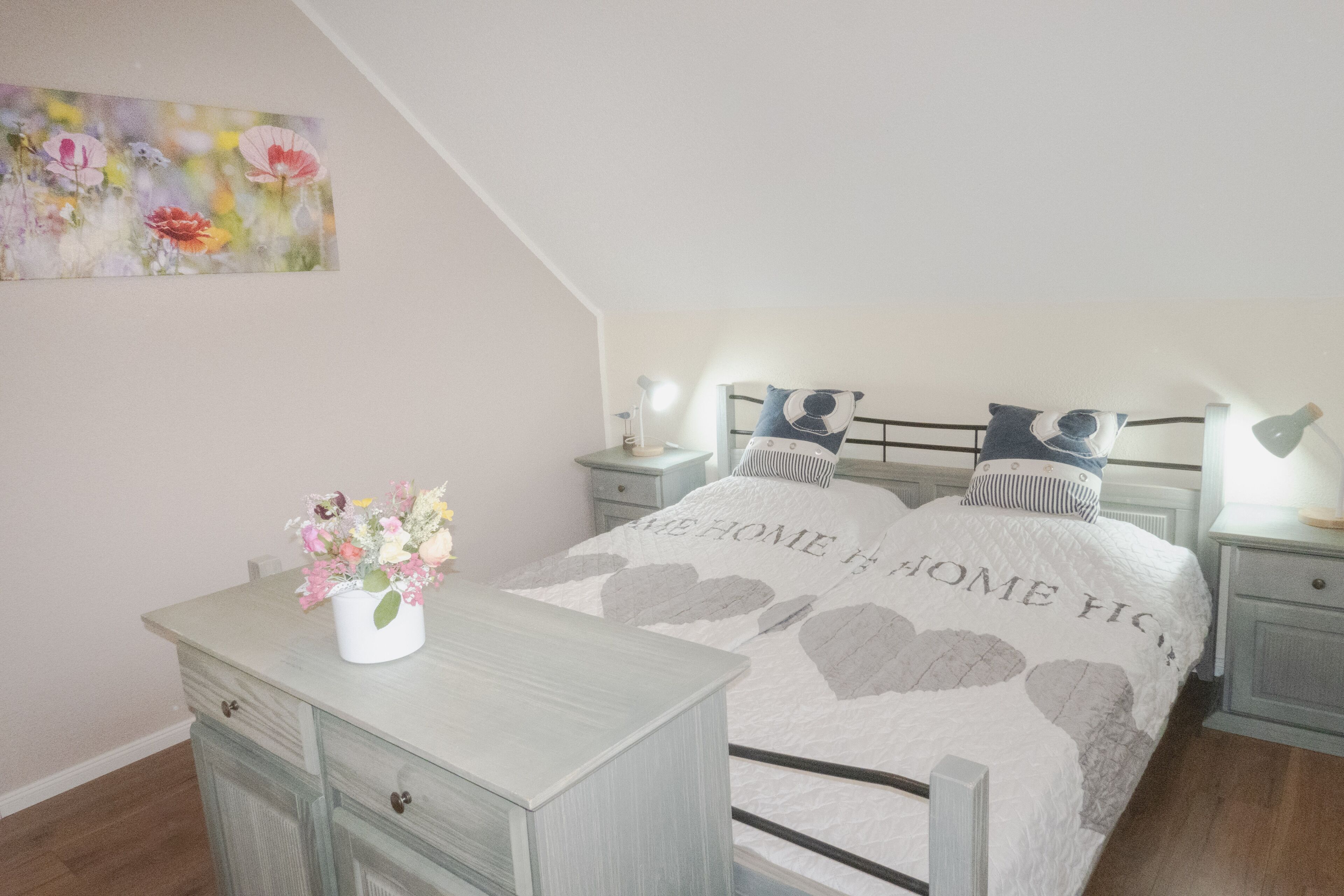 A bedroom with a bed, nightstands, a dresser, and a painting on the wall.