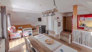 Un salon confortable avec un canapé, une table à manger avec un set de table, et un coin cuisine doté de meubles rouges et d’une cuisinière.