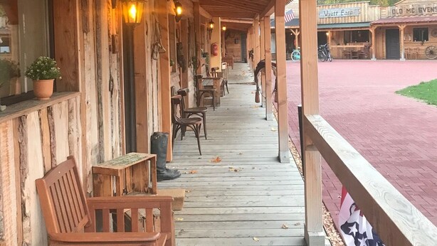 Une véranda en bois avec des tables et des chaises, un chemin pavé de briques rouges et une enseigne indiquant « Wyatt Earp ».