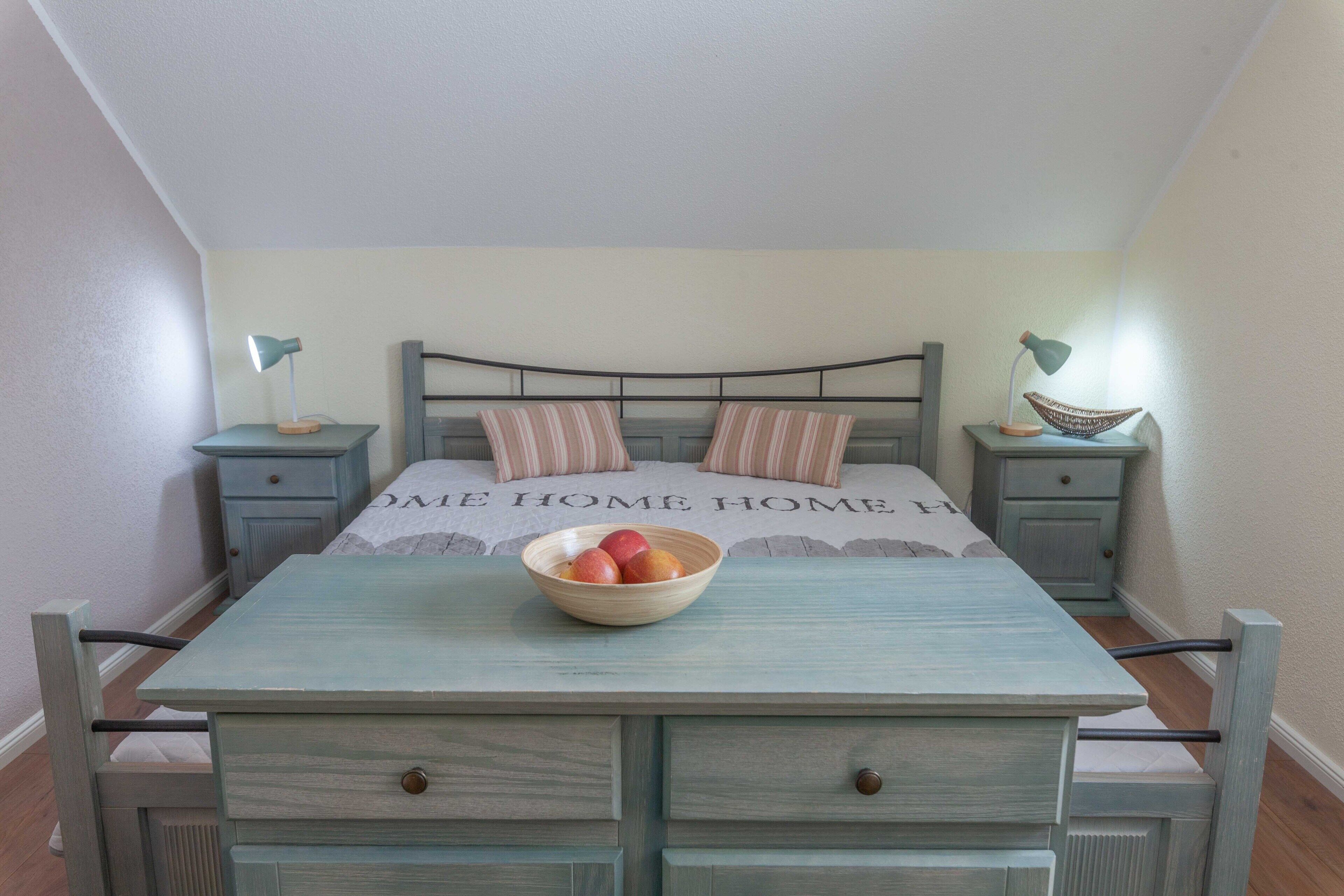 A bedroom with a bed, two bedside tables, a nightstand, a dresser, and a bowl of fruit on the dresser.