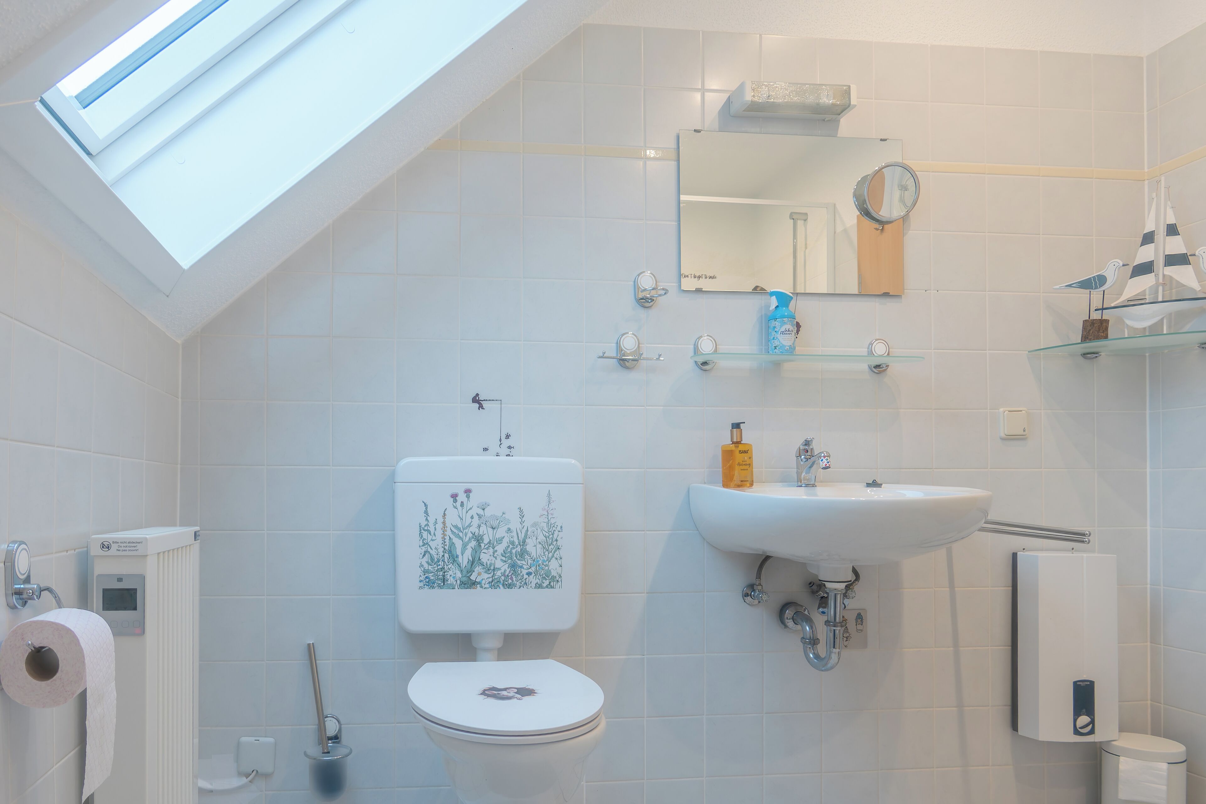 Un baño moderno con tragaluz, azulejos blancos, inodoro, lavabo y espejo.