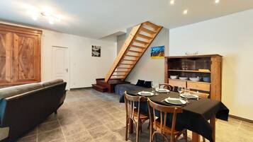 Comedor con una mesa dispuesta para cuatro, una escalera de madera y una estantería con vajilla.