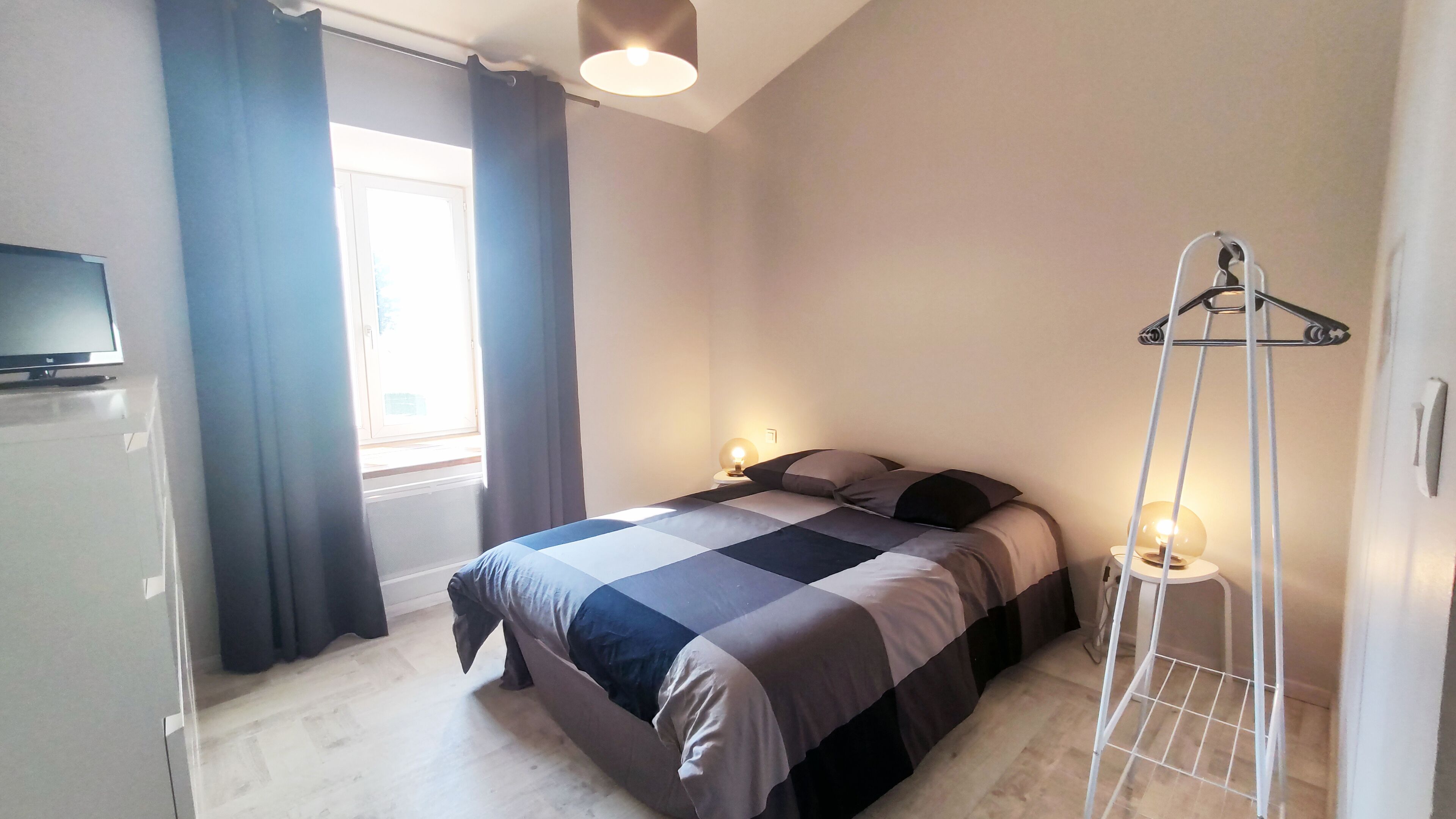A bedroom with a bed, bedside lamps, a TV, and a window with curtains.
