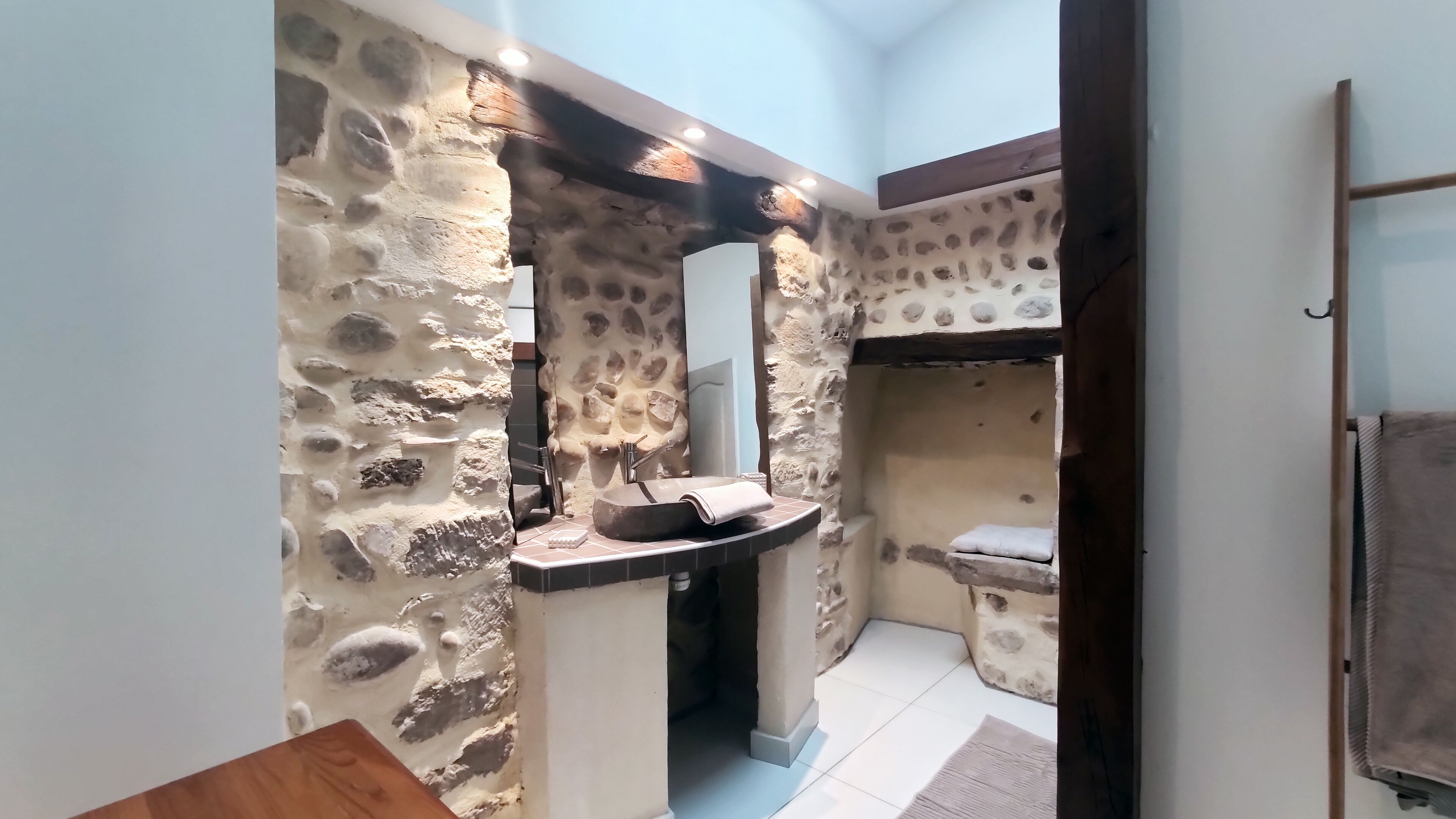 Une salle de bain avec un mur en pierre, un lavabo, un miroir et un porte-serviettes.