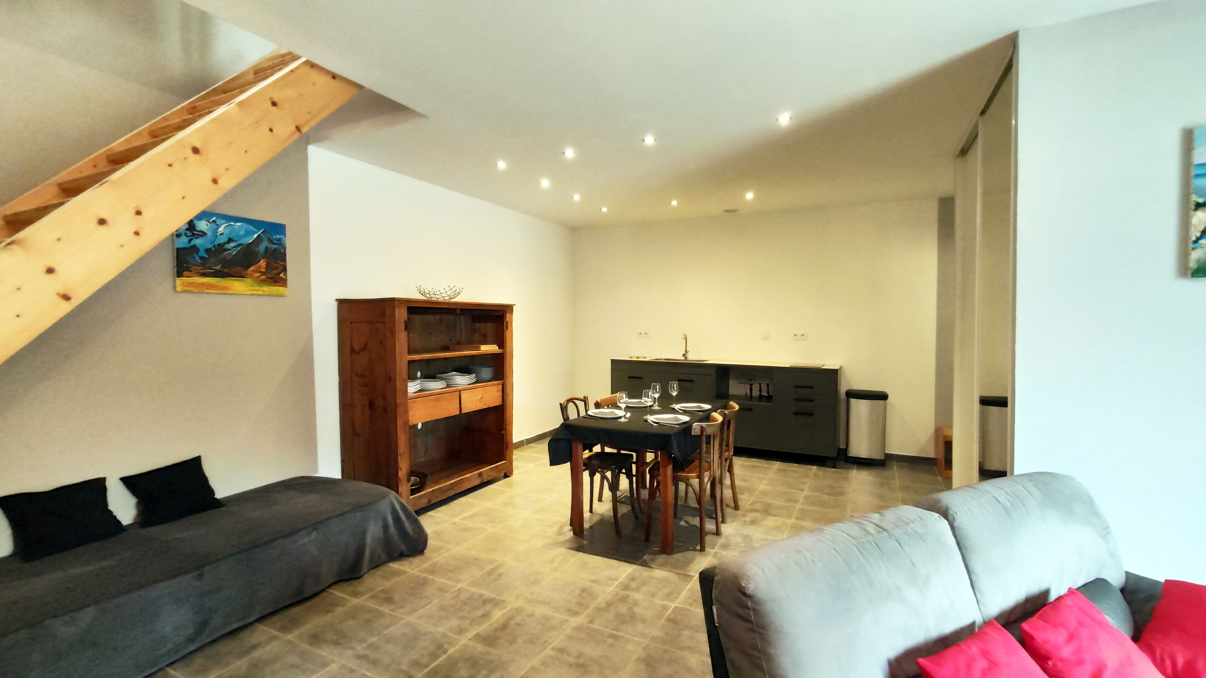 A living room with a sofa, a dining table set for four, and a kitchen area with cabinets and a sink.