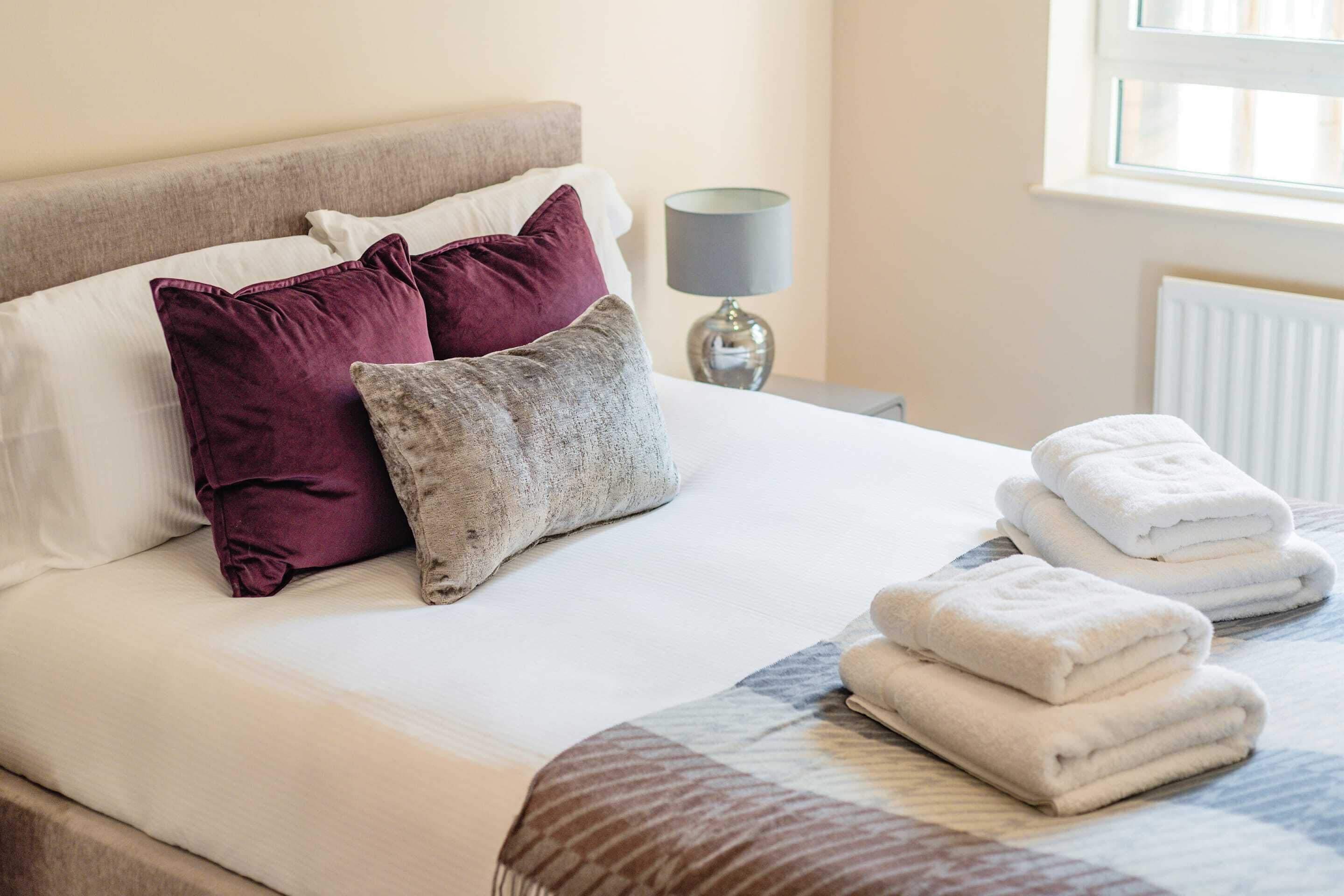 Een net opgemaakt bed met witte lakens, twee kussens en een opgevouwen handdoek.