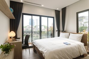 A modern hotel room with a large bed, a desk with a laptop, a chair, a globe, and a view of the city through large windows. - Mersey Central Hanoi Apart'Hotel (Hanoi)