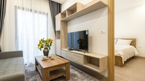 A modern hotel room with a bed, a TV, a wooden table with a vase of sunflowers, and a sofa. - Mersey Central Hanoi Apart'Hotel (Hanoi)