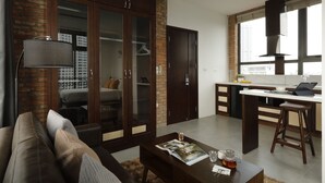A modern living room with a dark wooden cabinet, a glass door, and a sofa. There is a kitchen area with a bar stool and a window. - Mersey Central Hanoi Apart'Hotel (Hanoi)
