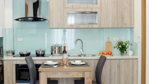 A modern kitchen with wooden cabinets, a stainless steel sink, and a dining area with a table set for two. - Mersey Central Hanoi Apart'Hotel (Hanoi)