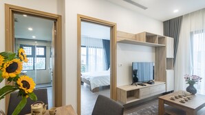 A modern hotel room with a wooden dining table, a sofa, a TV, and a bed with a white duvet. - Mersey Central Hanoi Apart'Hotel (Hanoi)